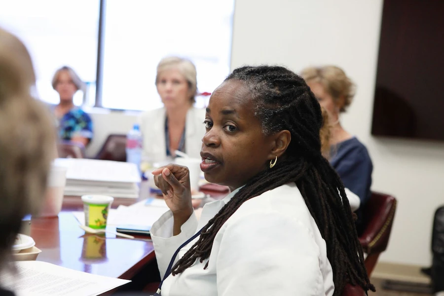 Female physician in a meeting room with other physicians.